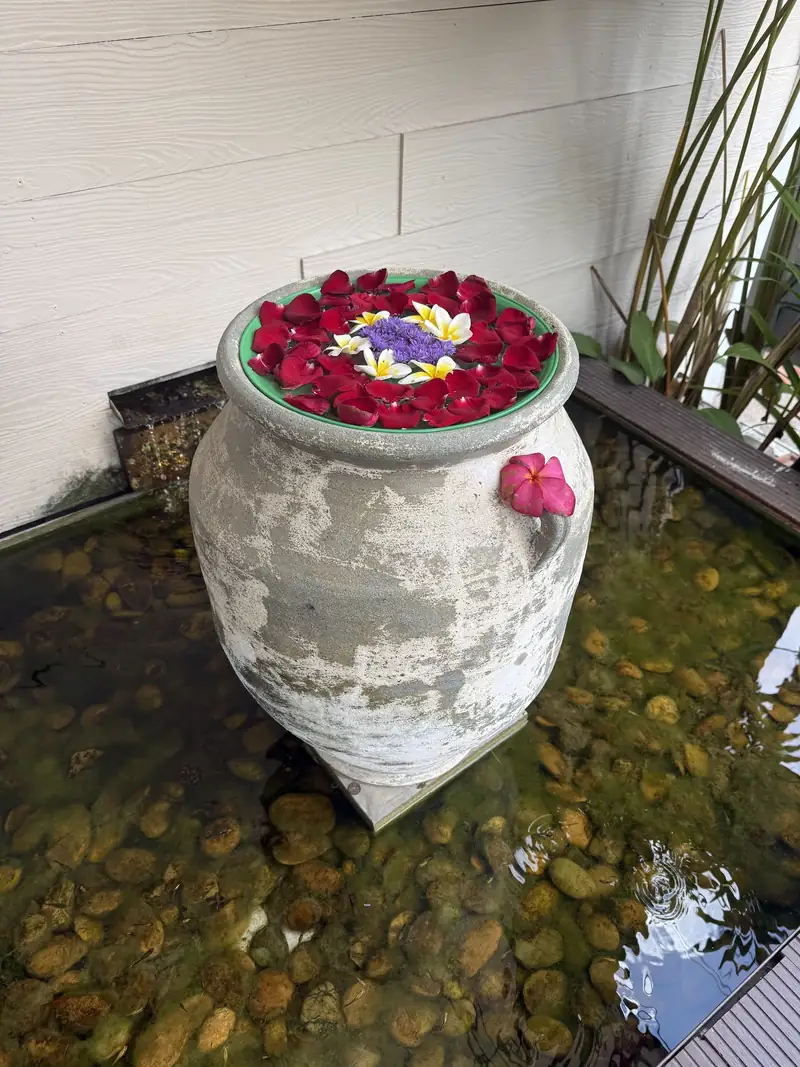 A stone jar topped with red and purple flowers in a pebble pond